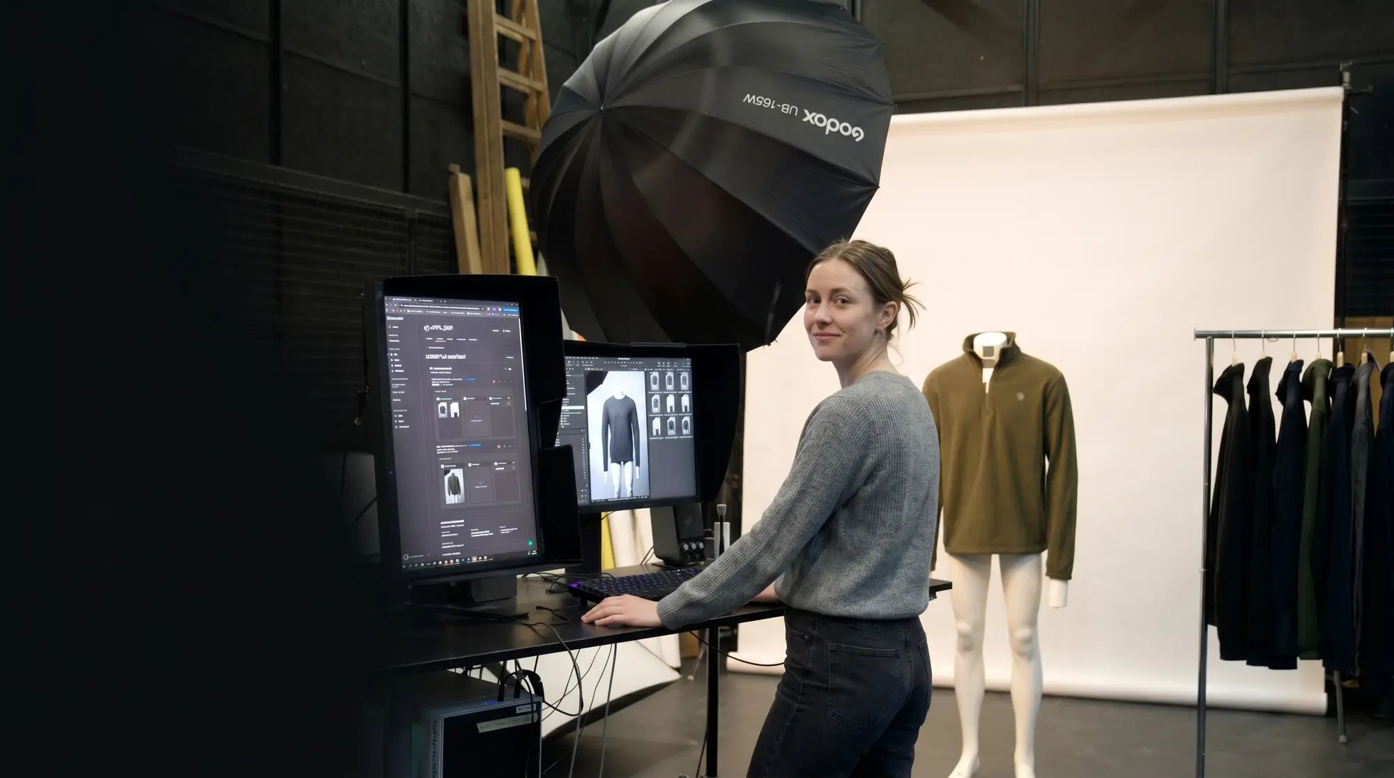 Photographer at a tethered workstation turns with a smile, while a product sample is ready on the mannequin in front of the sweep